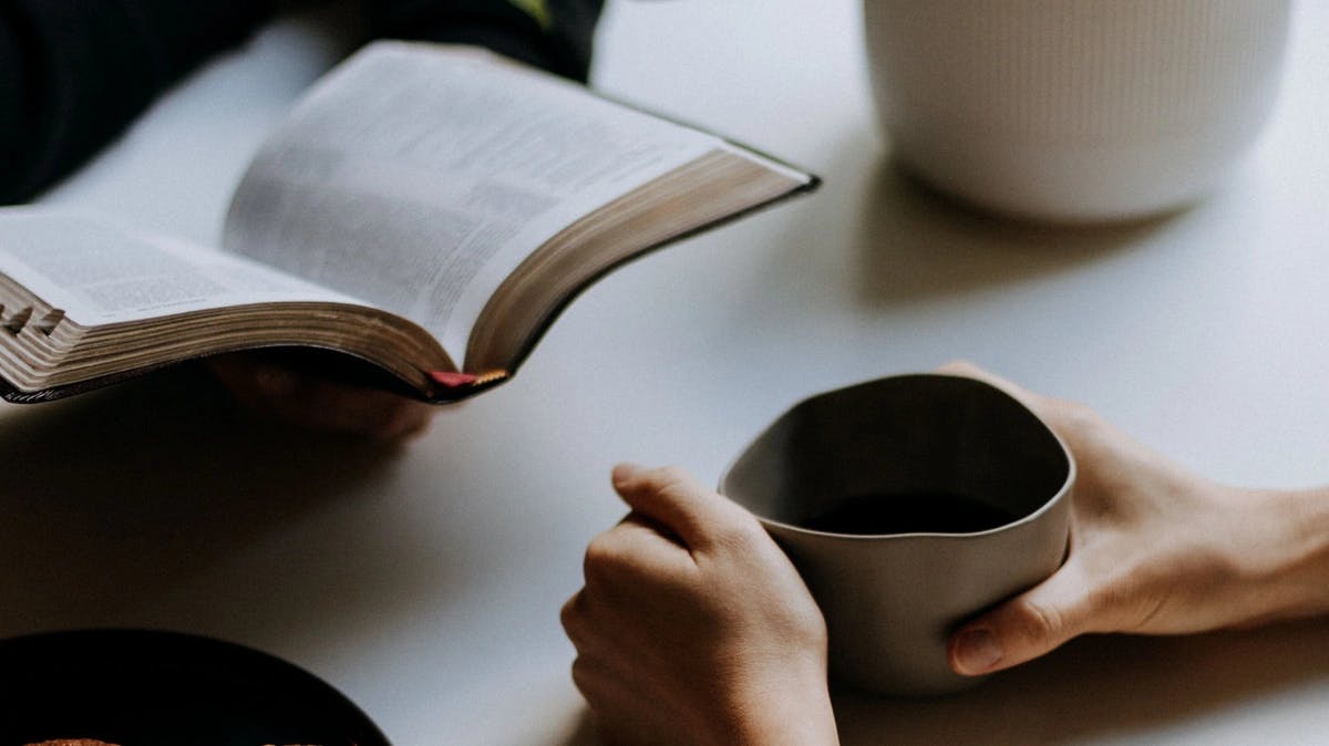 two people one holding an open Bible the other a ceramic mug