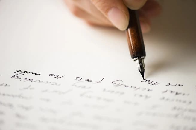 close up of hand writing on paper with fountain pen