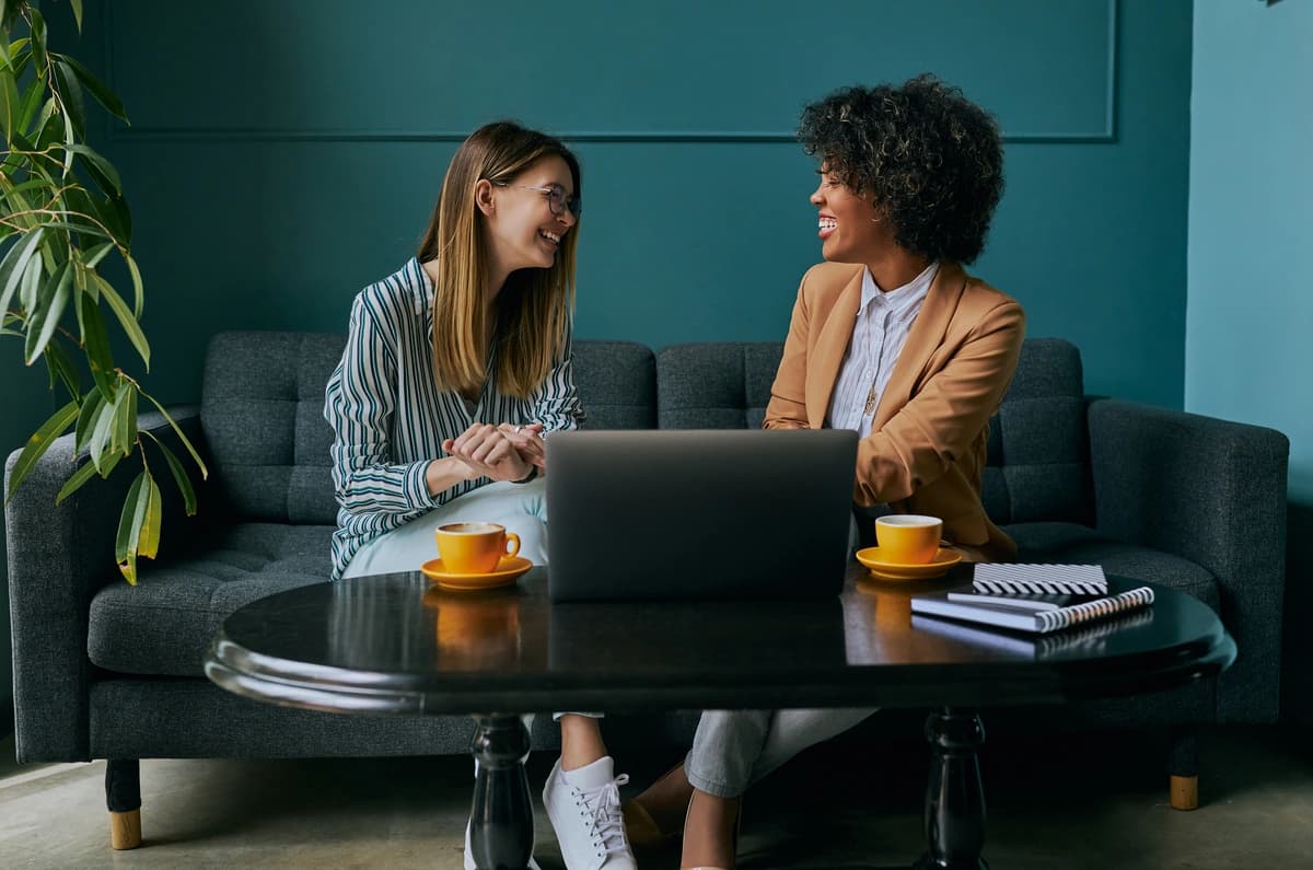 two women sitting down on a sofa having a conversation