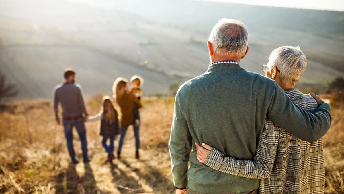 elderly couple with their arms around each other watching the rest of their family together in a field  