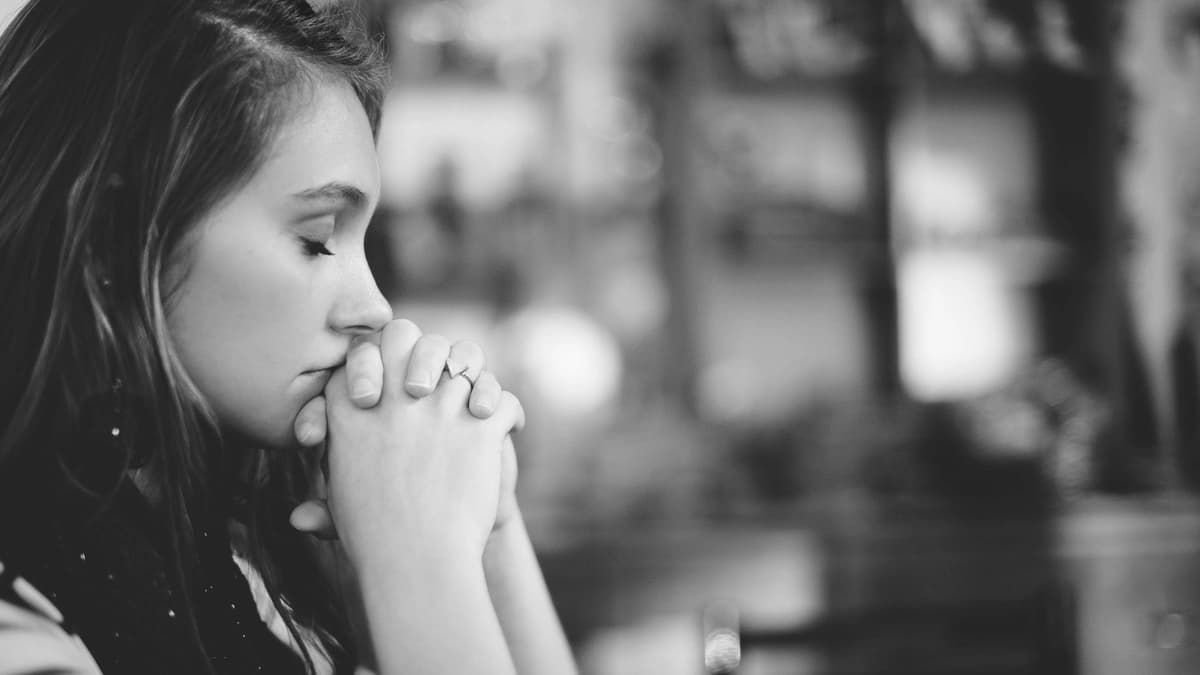 side profile of girl praying in church with hand folded and wresting on her chin, black and white